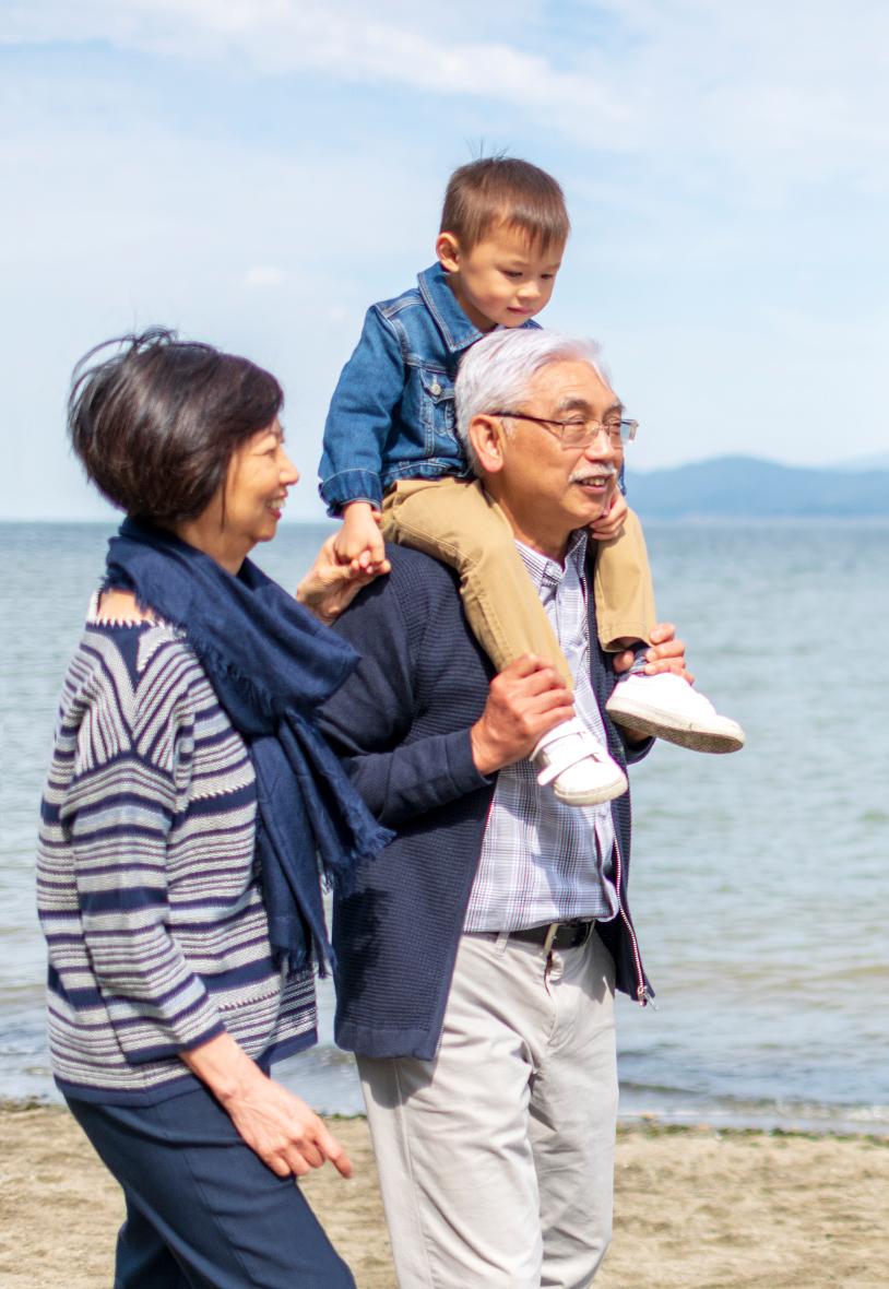 Grandparents waling on beach with grandson on shoulders