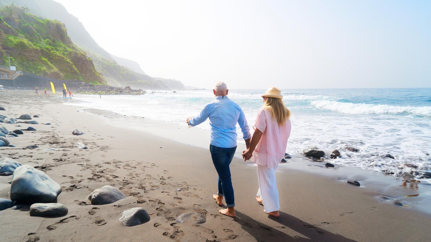 Older couple walking along tropical beach 