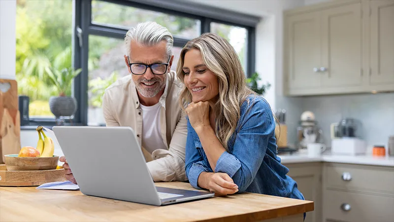 Couple sitting at kitchen table looking at their laptop