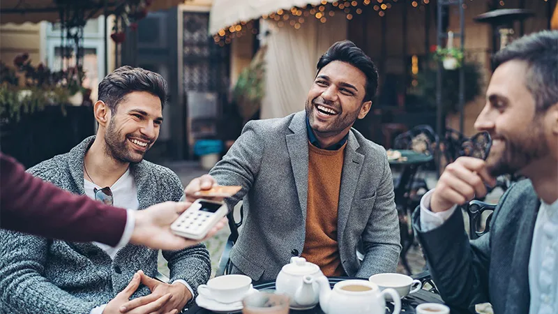 A man with his friends using his credit card to pay for a meal in a cafe