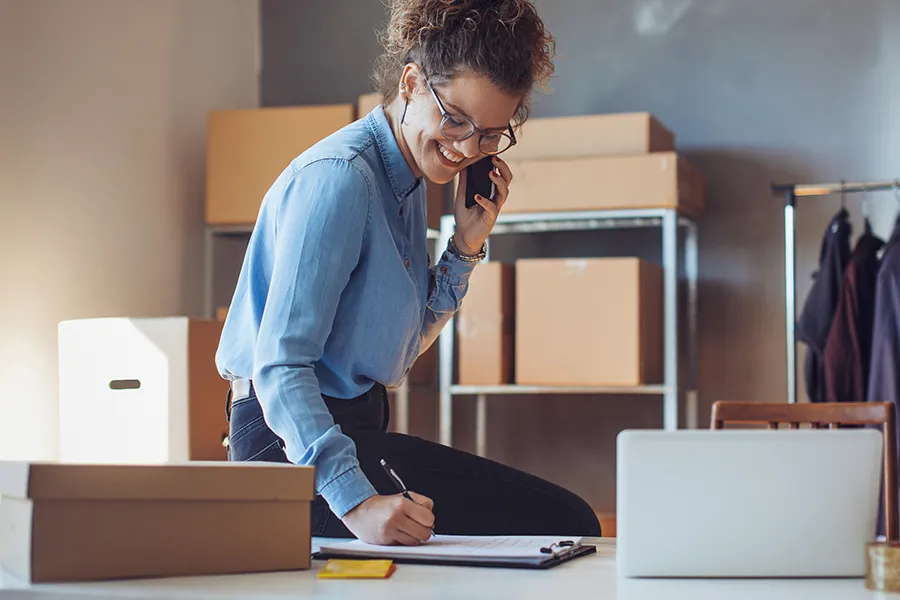A woman speaking on the phone while writing something down.